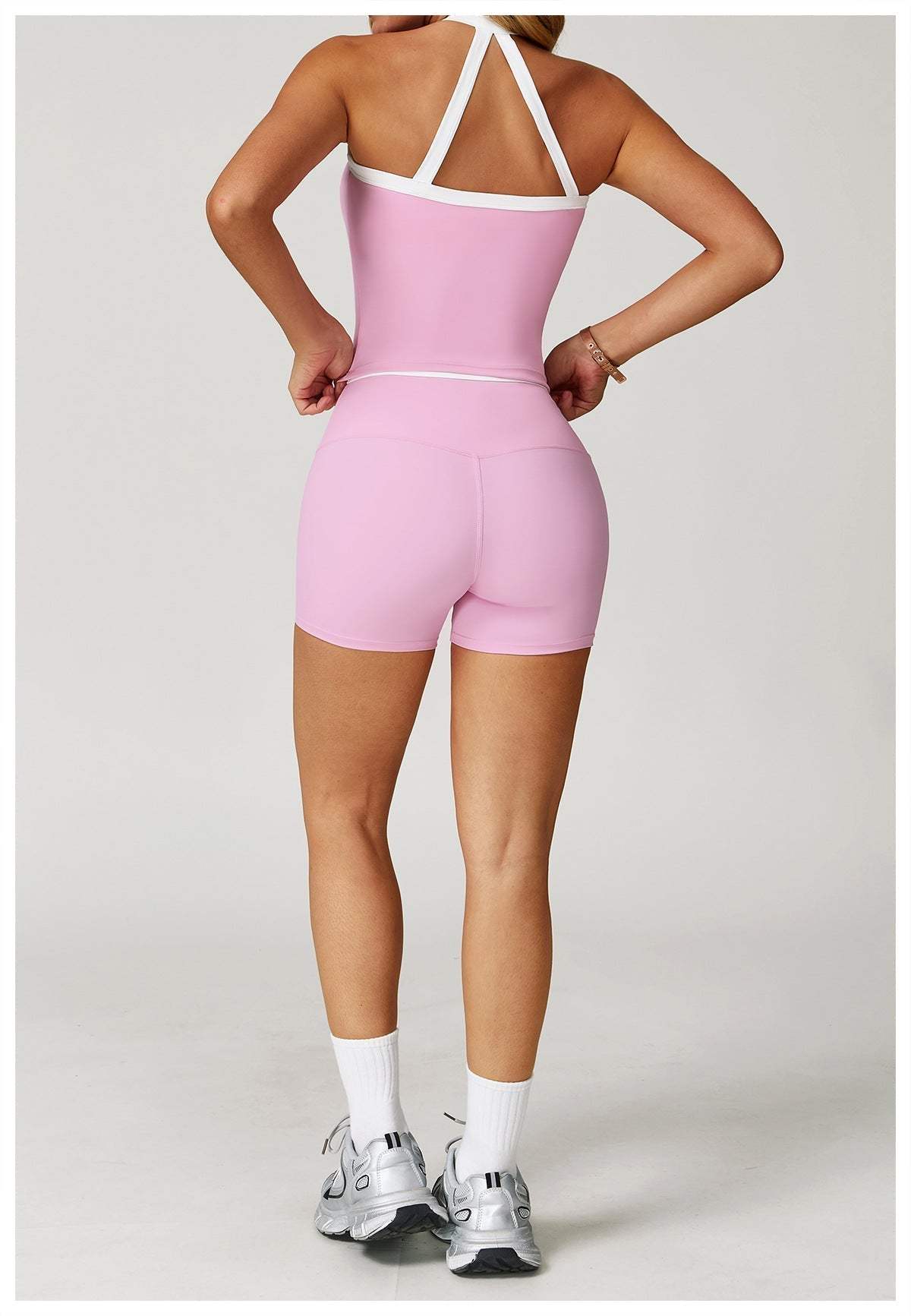Woman wearing pink high-waist gym shorts with white trim from back, athletic pose