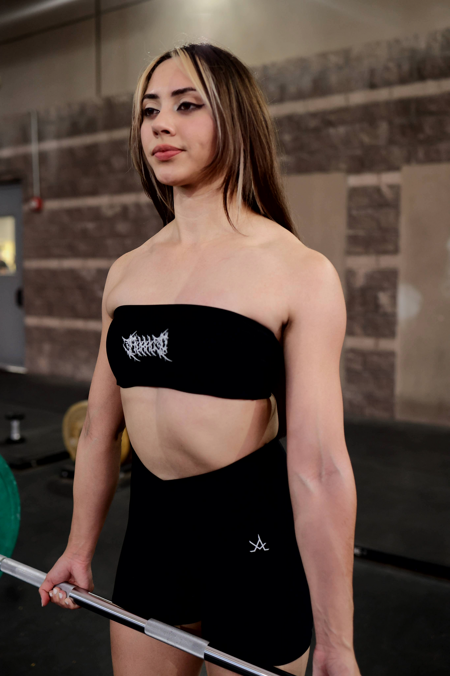Woman wearing black Aura Strapless Bandeau Bra and high-waist shorts in gym setting